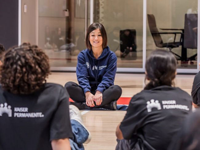 Woman sitting on yoga mat facing teens